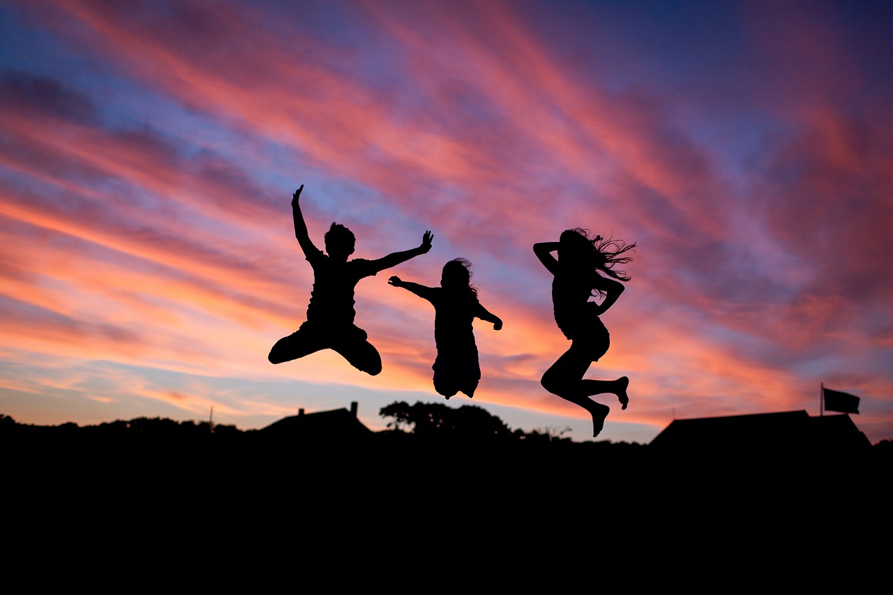 Three silhouettes of people jumping for joy with a colourful sunset in the background.